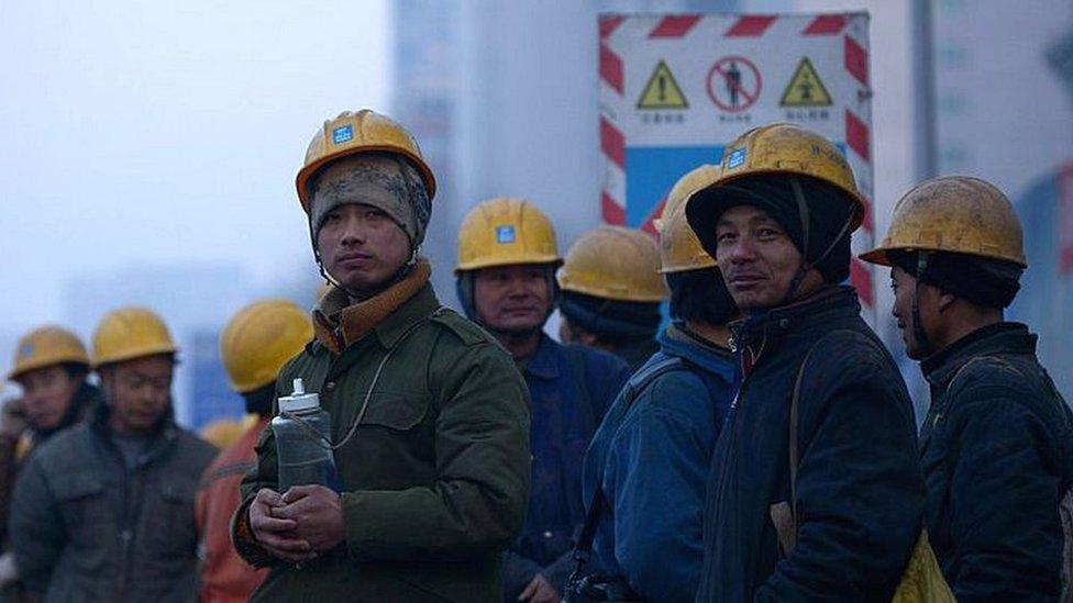 A group of Chinese workers wait for a shuttle bus outside a construction site in Beijing