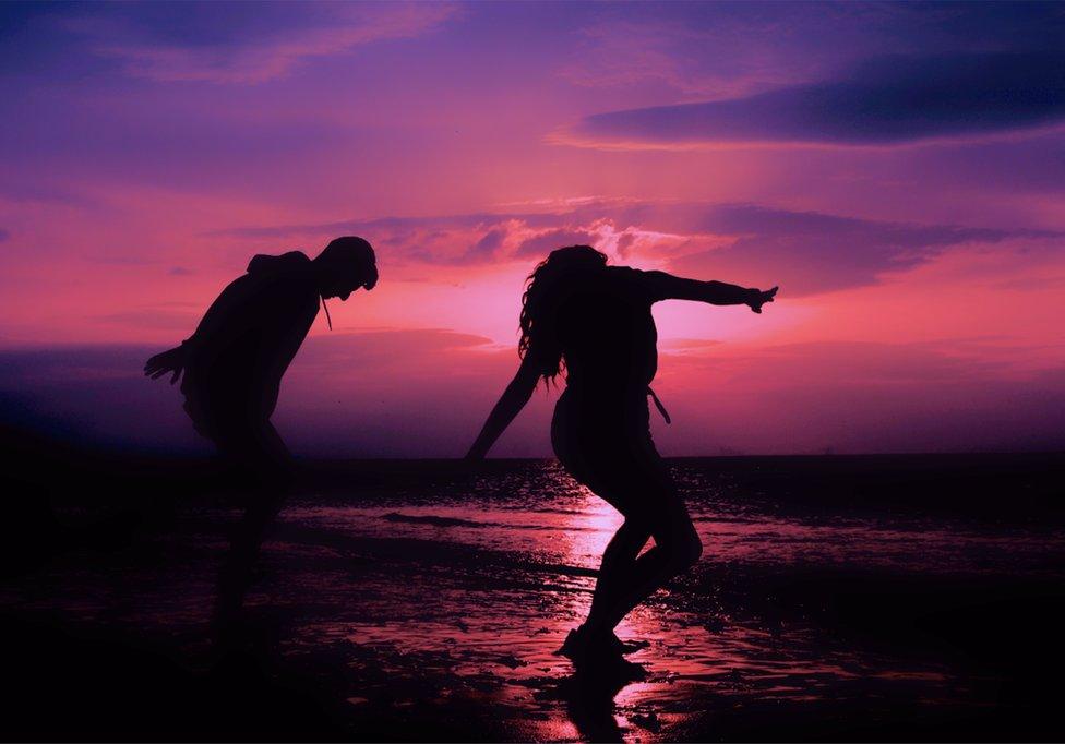 Two people dance under the pink sunset