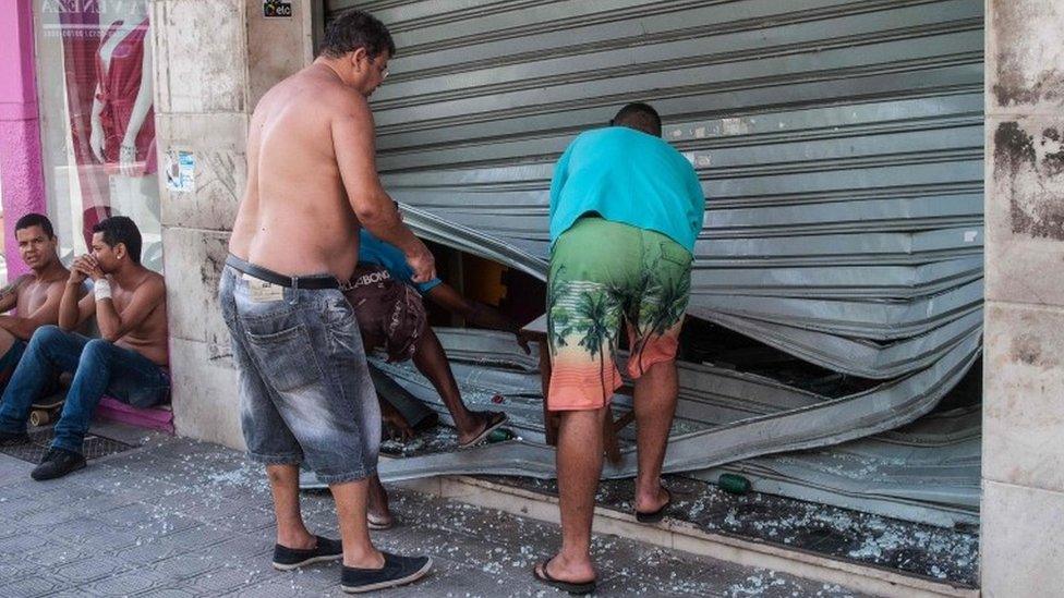 Men fix the broken shutter of their shop after burglars entered in Vila Velha, near Vitoria, eastern Brazil, on 6 February