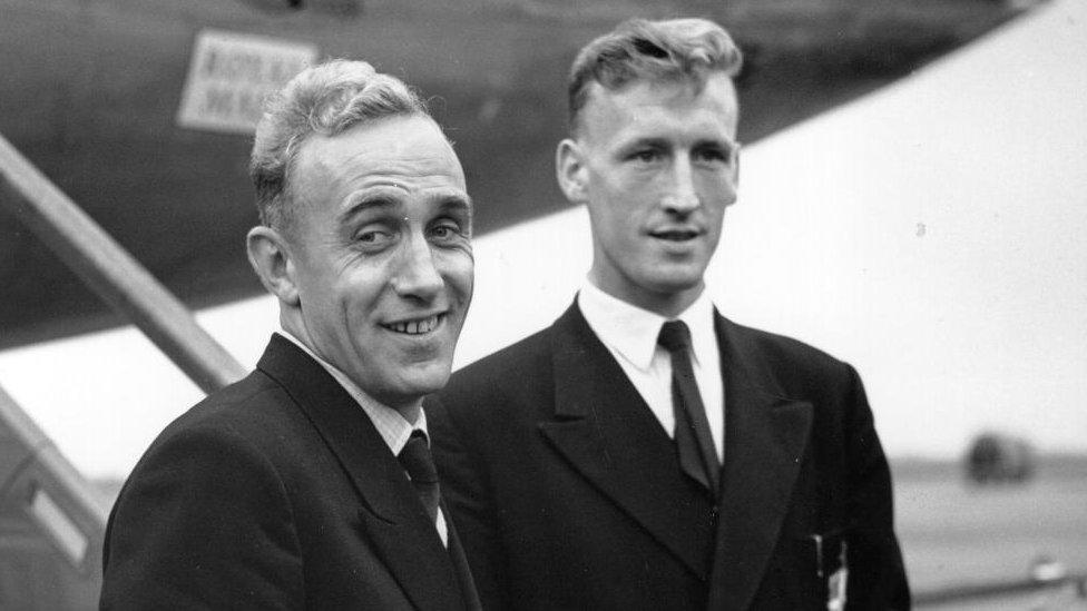 Ron Baynham and Billy Wright wearing suits stand outside an aeroplane