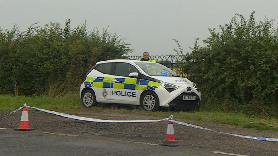 A police car parked off the road at the edge of the field