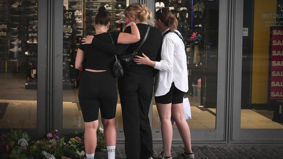 Three women lay flowers near the site of the shooting