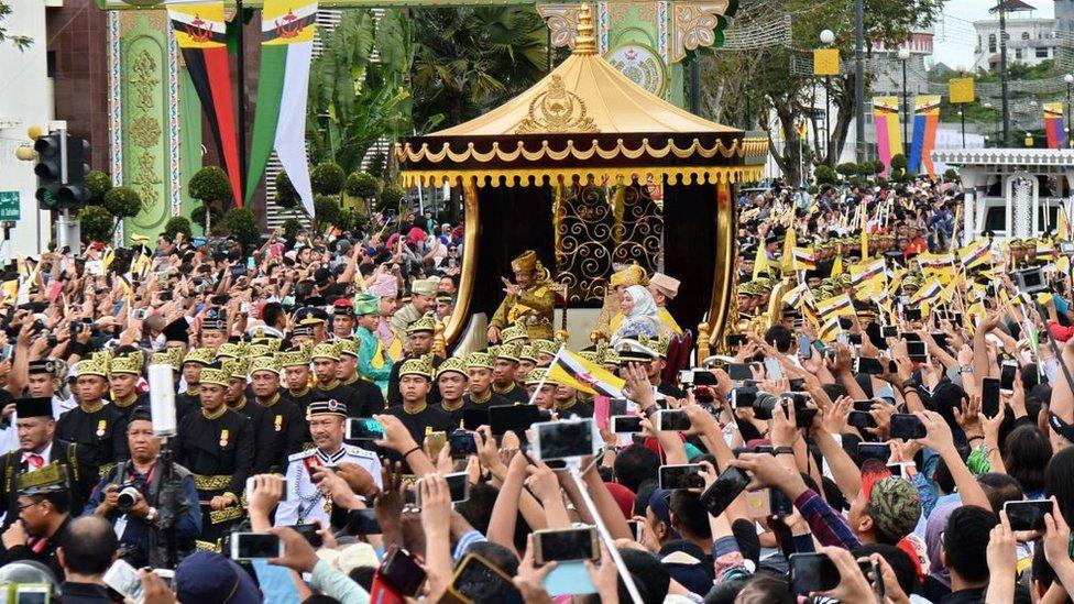 Brunei's Sultan Hassanal Bolkiah (center-L) and Queen Saleha (centre-R not visible) wave from the royal chariot during a procession to mark his golden jubilee of accession to the throne in Bandar Seri Begawan on October 5, 2017