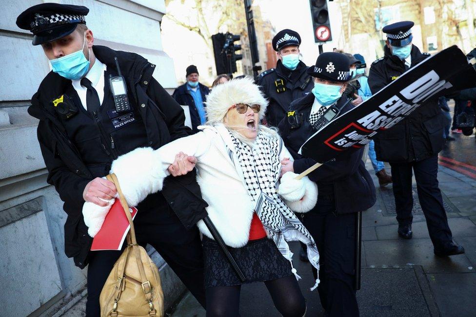 Police officers detain a woman holding a placard outside the Westminster Magistrates Court as Julian Assange's lawyers seek bail for their client in London, 6 January 2021.