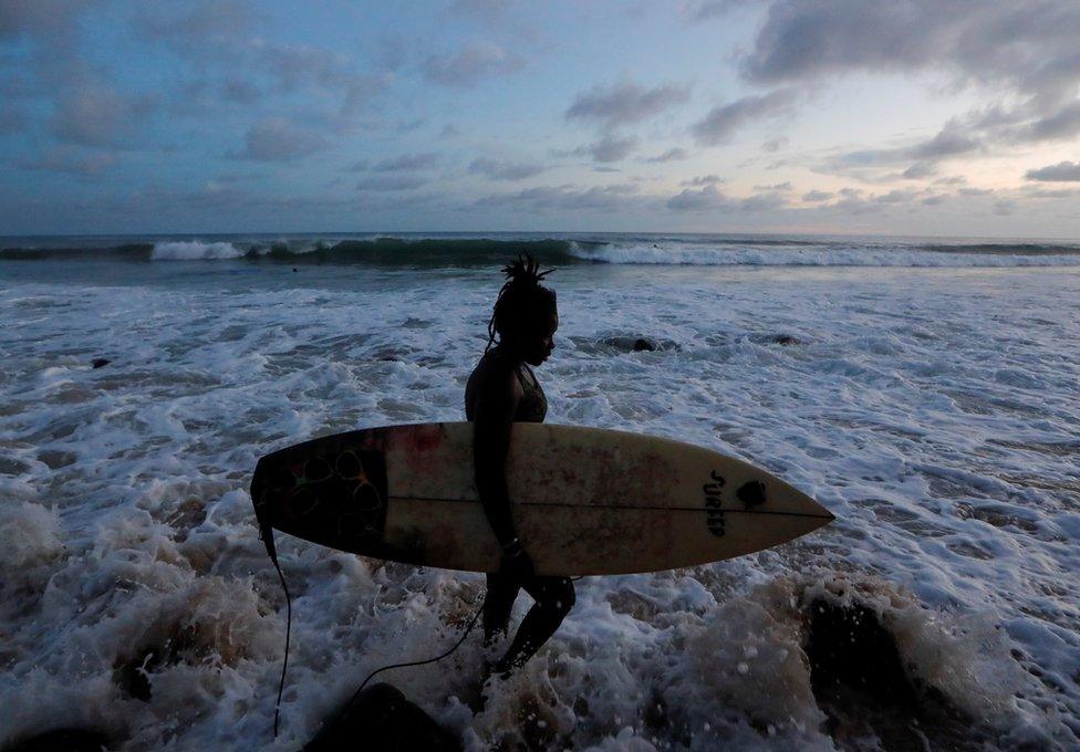 Khadjou Sambe walks in the water holding her surfboard