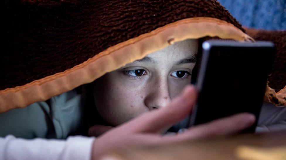 girl-hiding-under-a-blanket-looking-at-her-phone