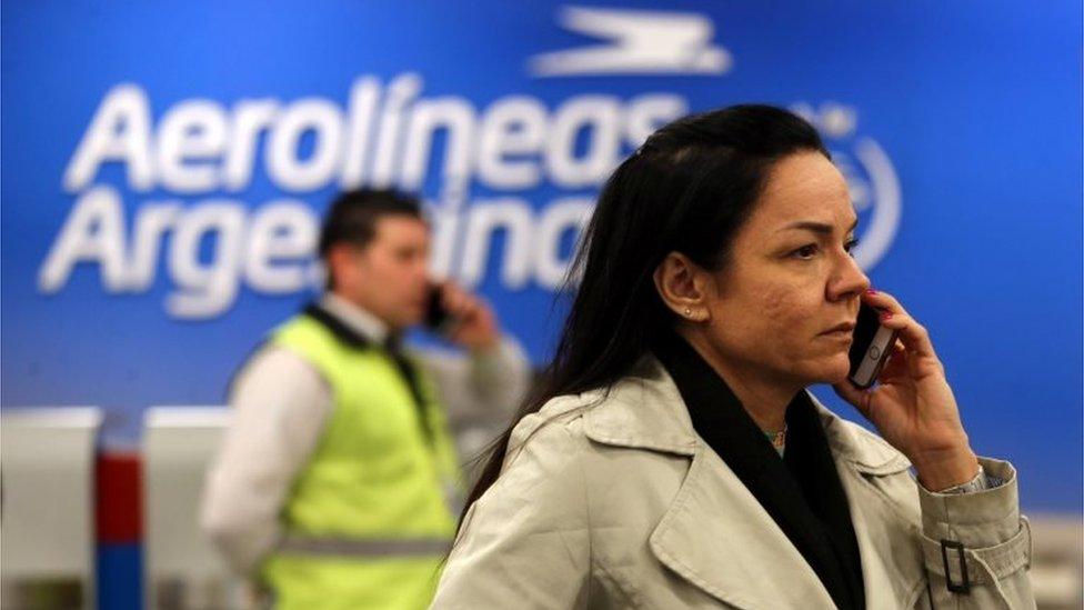 A passenger uses her cell phone in front of an airport security officer at a closed counter of Argentina"s flagship air carrier Aerolineas Argentinas at Buenos Aires airport, Argentina October 31, 2017.