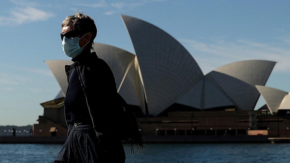 A pedestrian wearing a face mask walks past the Sydney Opera House in Sydney on 13 July 2021