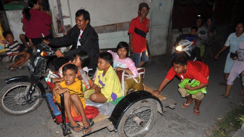 Residents of Padang ride on a scooter and sidecar as they rush to higher ground