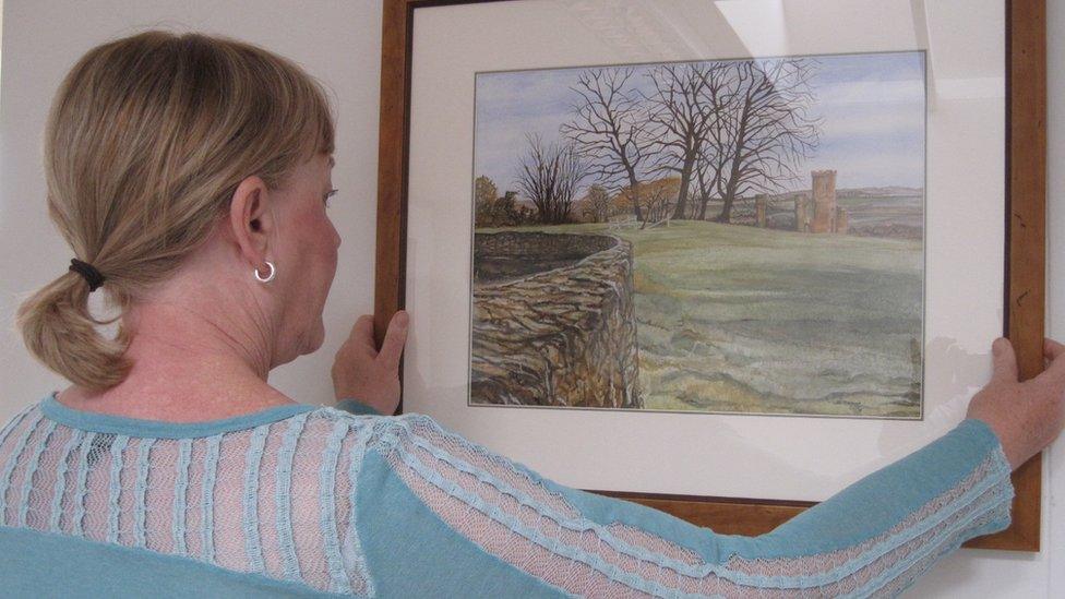 Dorothy Taylor hangs a painting on the wall