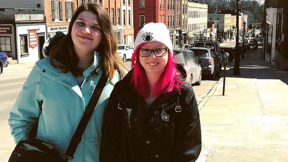 Two girls smiling at the camera. Behind them is a metropolitan street.