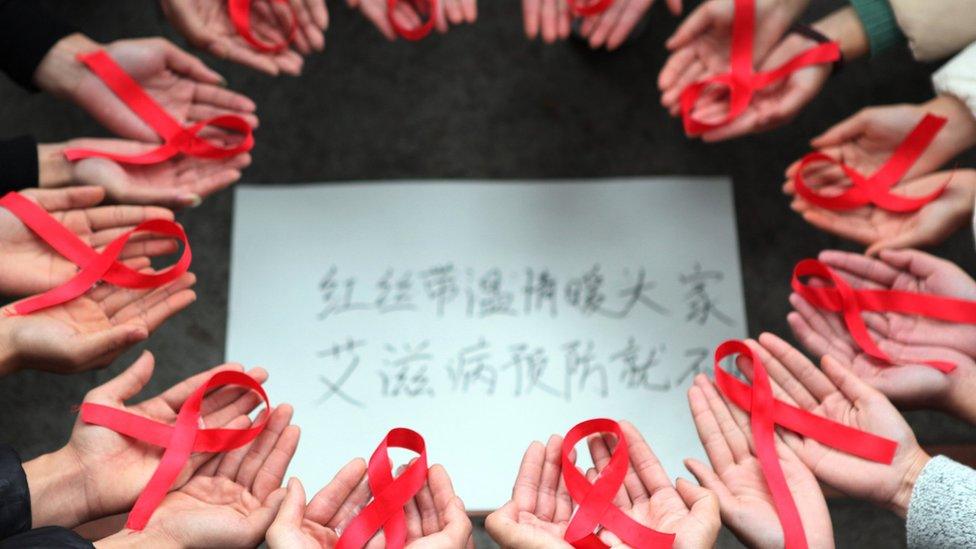 This picture taken on 30 November 2015 shows volunteers holding red ribbons above a piece of paper written in Chinese that reads ''Red ribbons bring warmth to everyone to prevent AIDS' during an event for World Aids Day in Chongqing