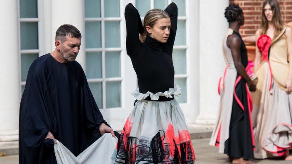 Grace Jabbari in black turtleneck and long grey skirt with elbows raised