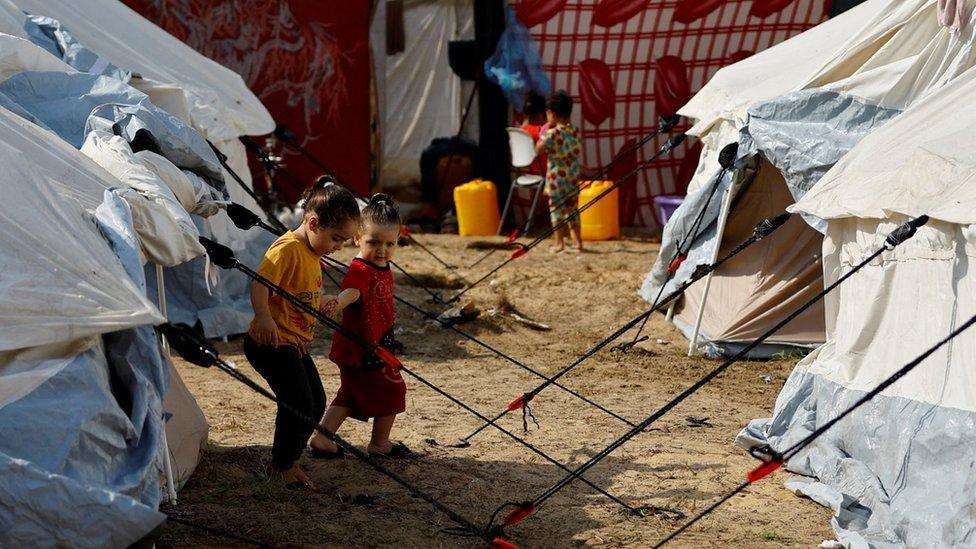 Displaced Palestinian children walk inside a tented camp at a UN-run facility in Khan Younis, in the southern Gaza Strip (24 October 2023)