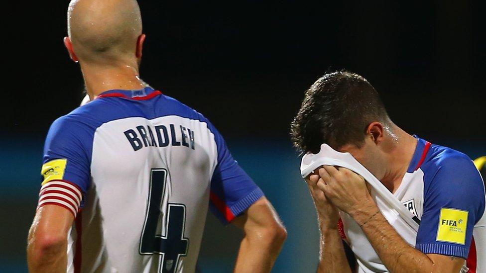 A USA footballer holds his jersey to his face while his teammate looks on.