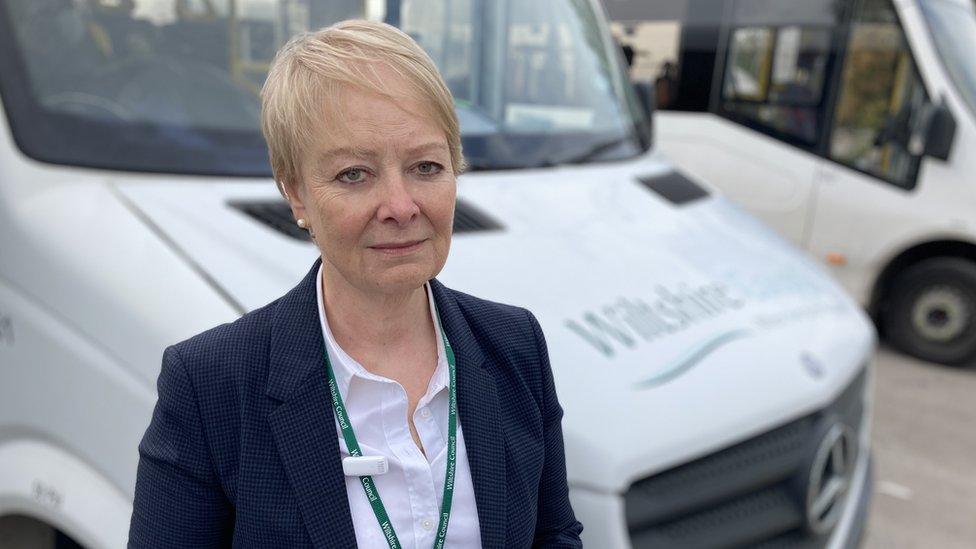 Councillor Caroline Thomas stands in front of one of the seven damaged minibuses with a smashed windscreen. She has a concerned look on her face.