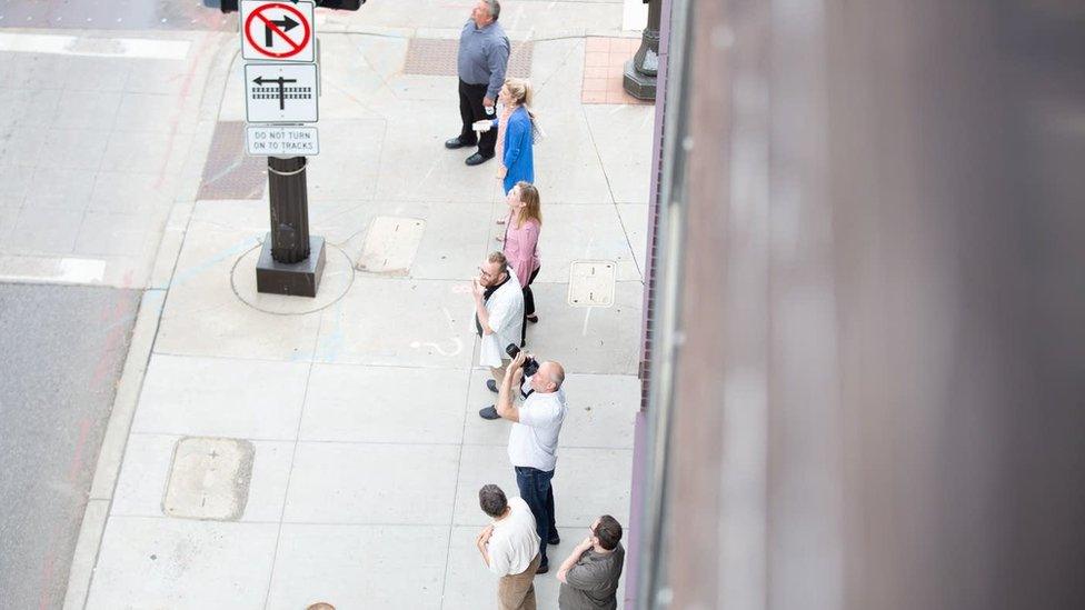 Crowds photographing the building and looking upwards on the street