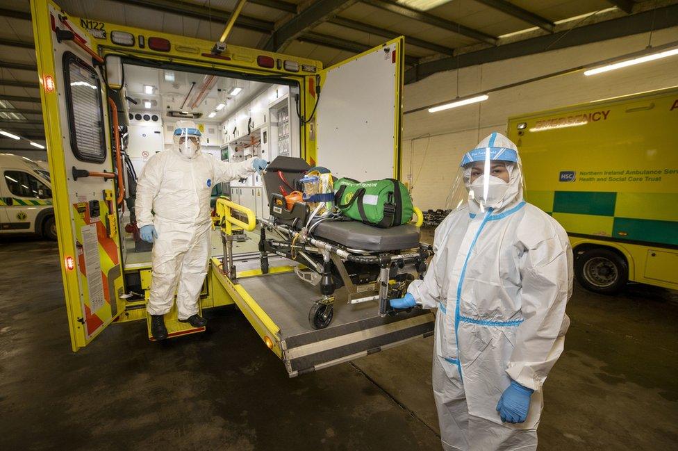 Paramedics wearing protective equipment remove a trolley bed from an ambulance