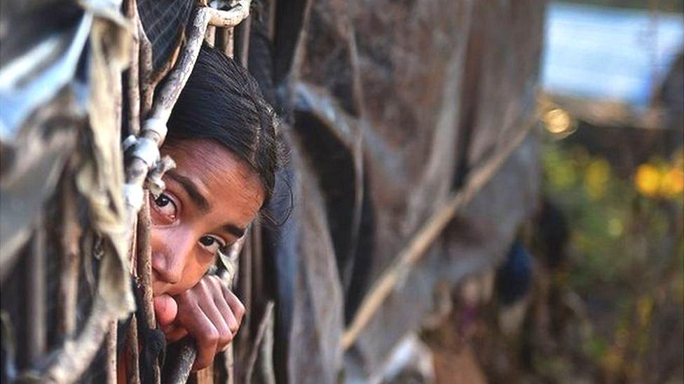 girl looking out from a makeshift shelter