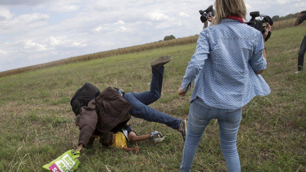 A migrant carrying a child falls after Ms Laszlo trips him