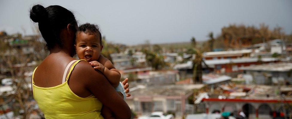 Image shows a woman carrying her son while looking at the damage after Hurricane Maria in Canovanas, Puerto Rico