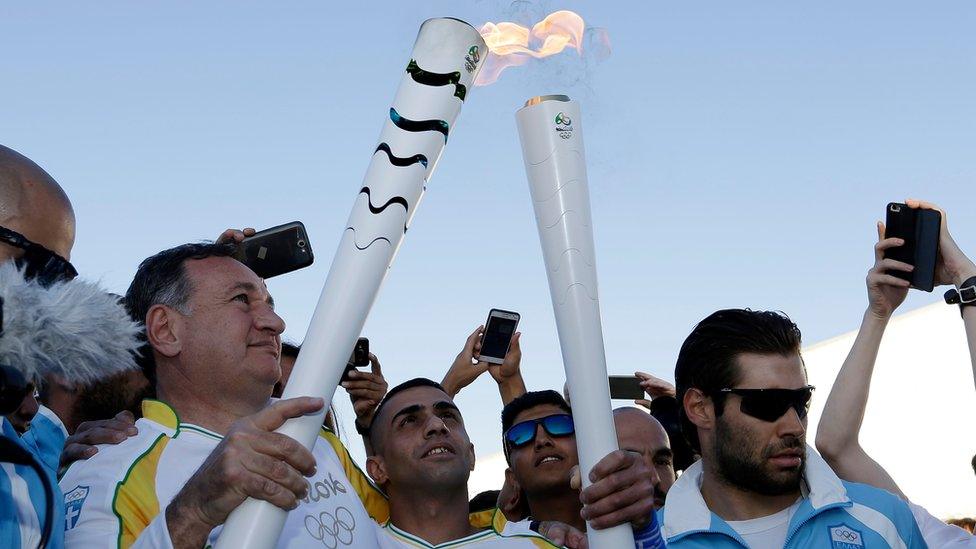 Ibrahim al-Hussein (centre) receives the Olympic flame at the Eleonas refugee camp