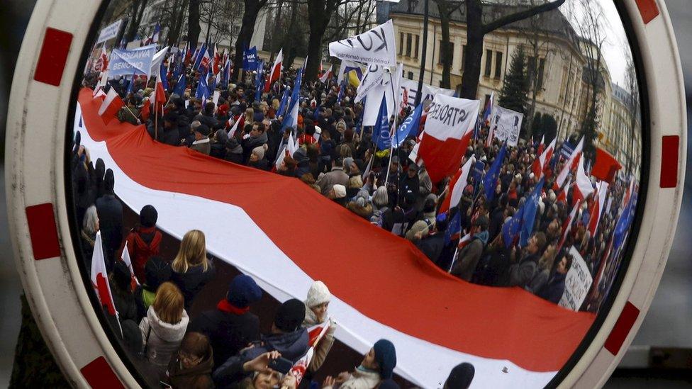 People holding a giant Polish national flag are reflected in a mirror as they take part in a march demanding their government to respect the country's constitution in Warsaw, Poland (12 March 2016)