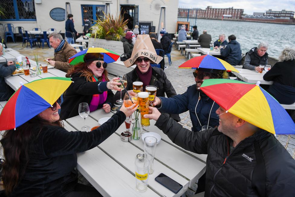 Drinkers toast with drinks whilst wearing umbrellas on their heads