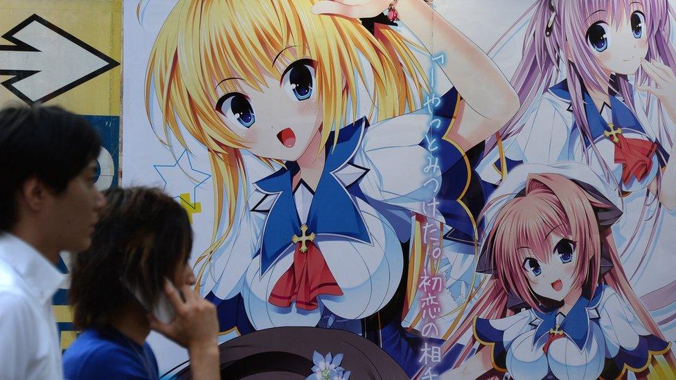 People walk past pictures of anime characters on a wall in Tokyo