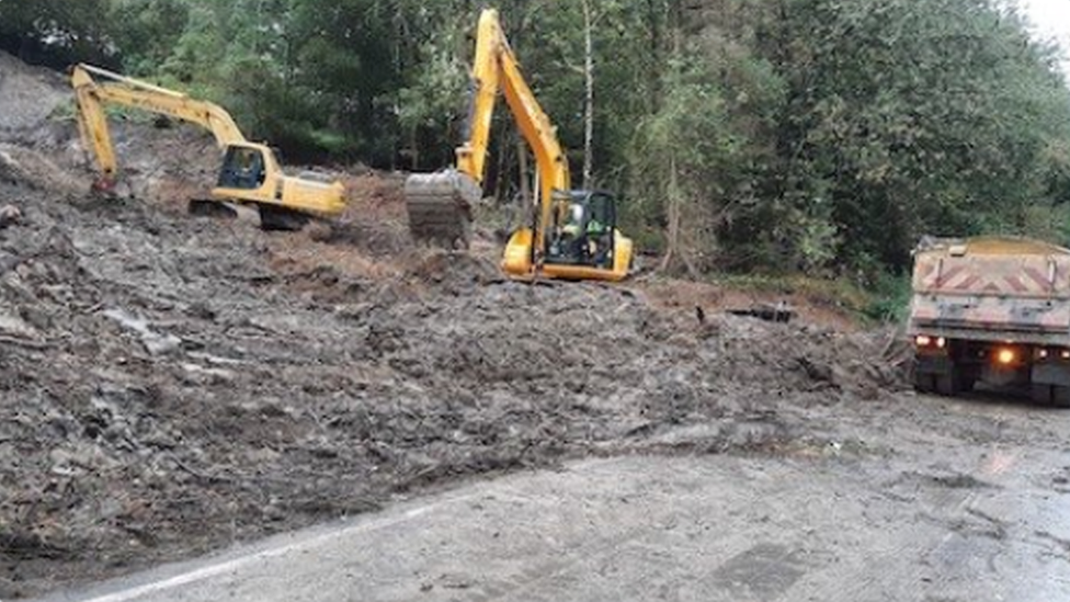 Two diggers and a truck on a landslide-hit road