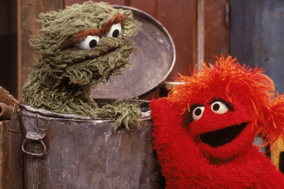 A red muppet visits Oscar the Grouch, inside his garbage can, in a scene from "Sesame Street" in the 1980s.