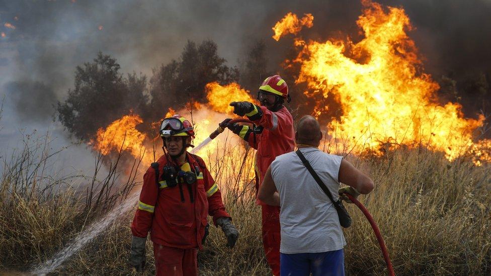 Firefighters and volunteers try to extinguish the fire broke out at forested land in Penteli town of Athens, Greece on July 23, 2018