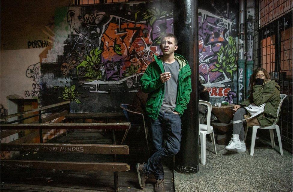 A young man stands in the smoking area of a nightclub