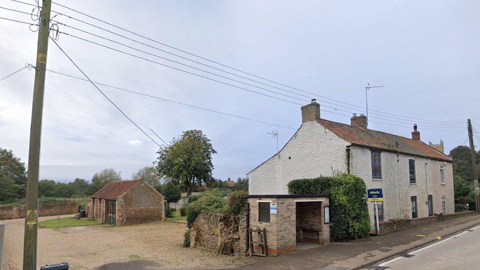 White-rendered two-storey house with driveway and outbuildings alongside a main road