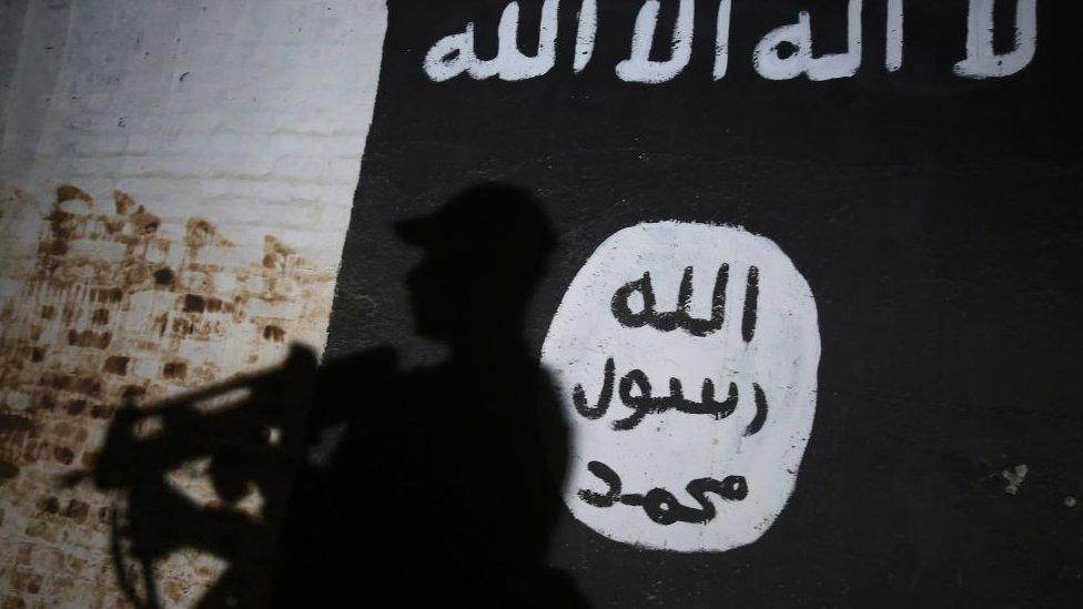 A soldier walks past a mural bearing the logo of the Islamic State (IS) group