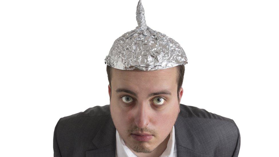 A man with a tin foil hat stares at the camera, suspicious of it.