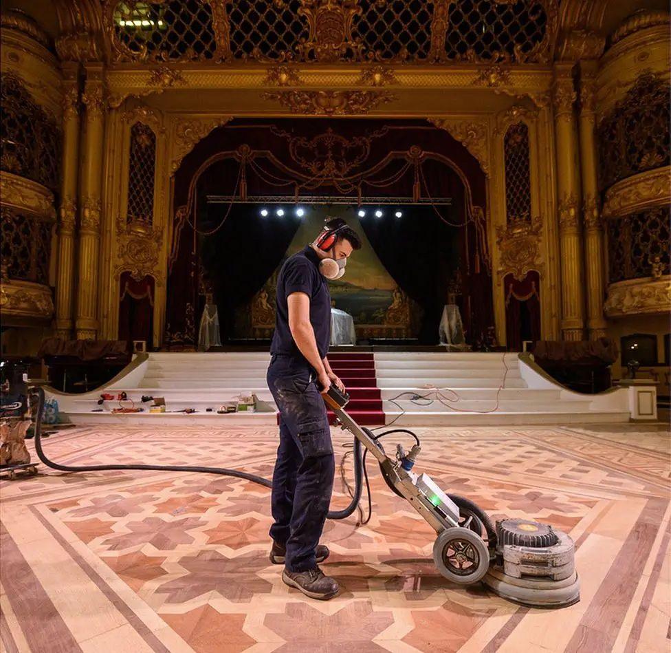 A man in a dust mask sanding the ballroom floor.