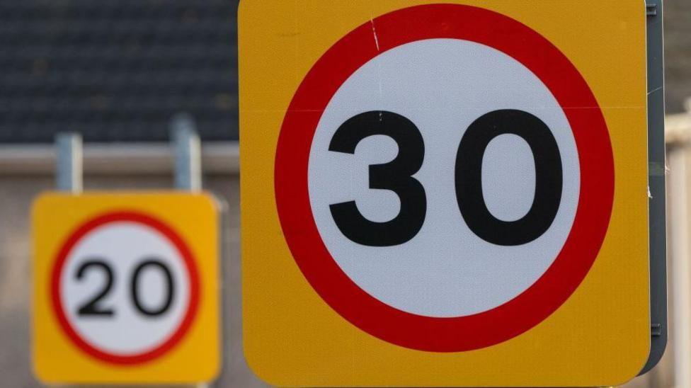 A 30mph speed limit sign in front of a 20mph speed limit sign