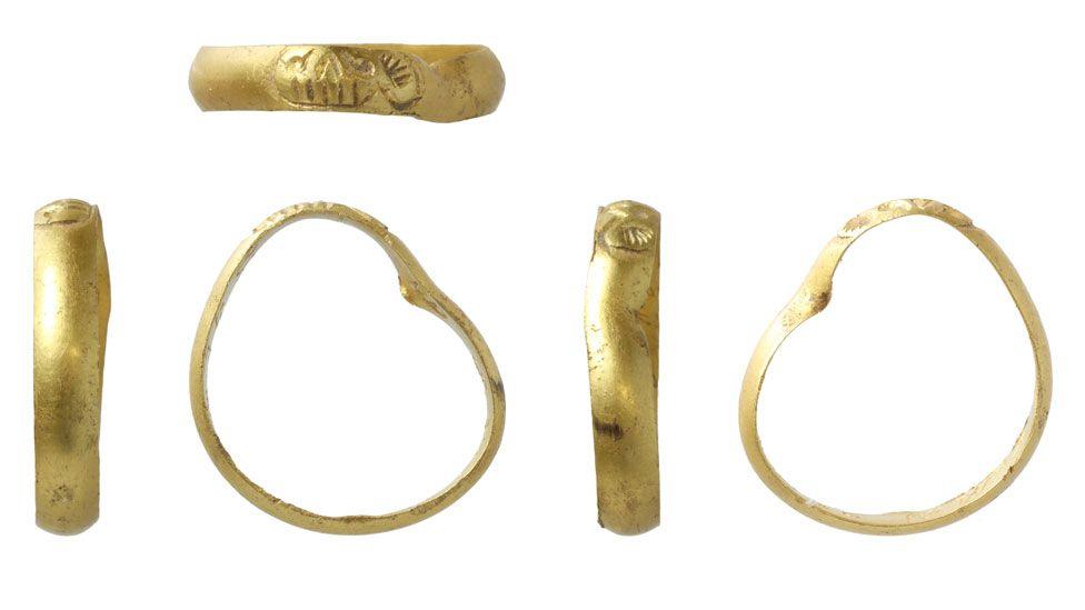 Five views of 17th Century gold mourning ring, four in a row and one view showing a side of the band above the others. The ring's outer band has a stylised skull bezel design. The ring has become misshapen, resembling a bean in shape