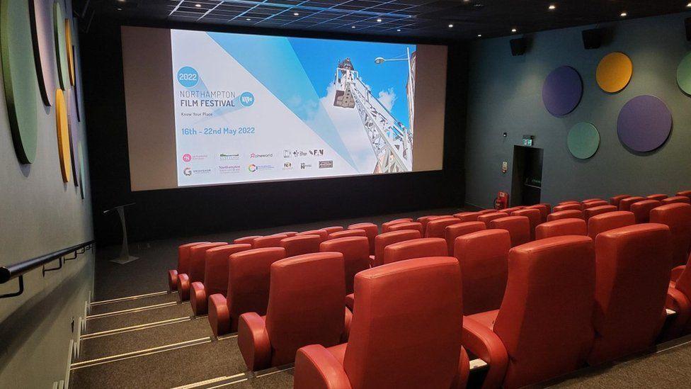 The inside of a cinema with red chairs and steps down to the screen, which is showing a Northampton Film Festival slide.