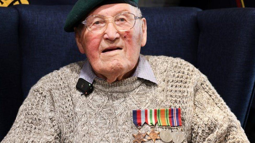 Jeffrey Broadhurst in an oatmeal coloured jumper with row of medals pinned on the right side of his chest. He is looking at the camera and wearing clear glasses and a beret.