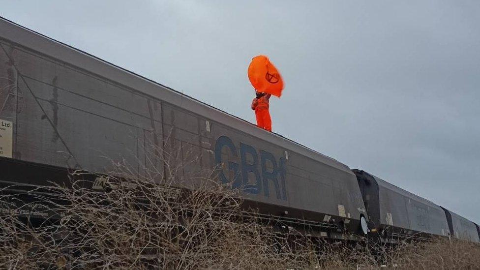 Activist wearing orange suite waving an orange flag on top of a train