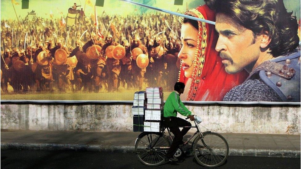 A cyclist rides past a giant poster of Jodhaa-Akbar