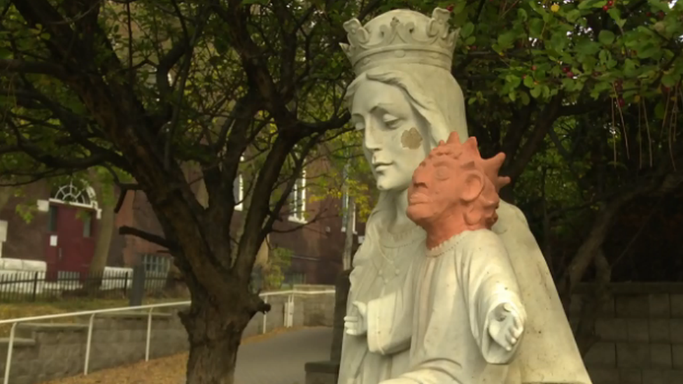 A view of the white statue of Mary and baby Jesus with the orange replacement head