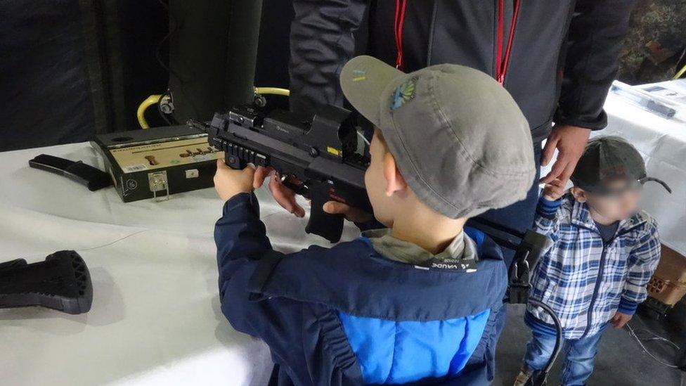 A photo from the event showing a young boy holding a military-style gun