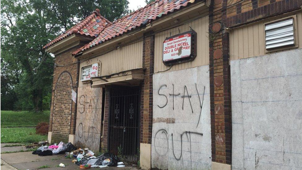 Boarded up building with piles of rubbish outside, and the words "Stay Out" in spray paint.