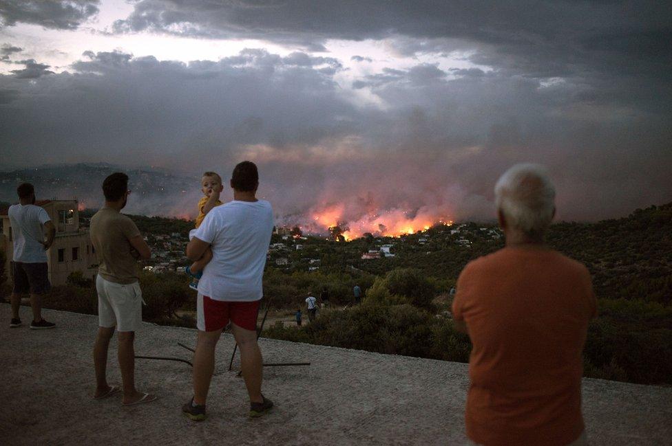 People watch a wildfire in the town of Rafina, near Athens