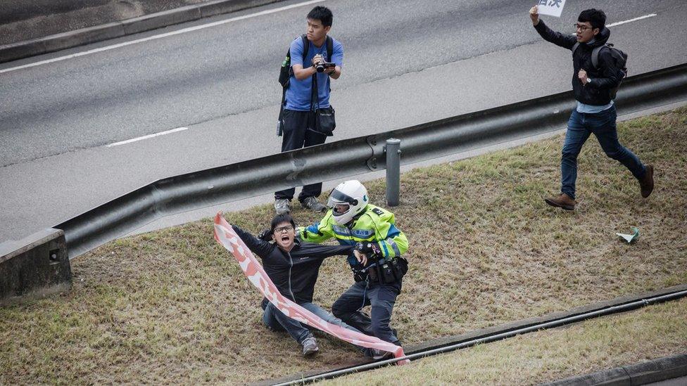 A student activist holding a banner is approached by a traffic police officer