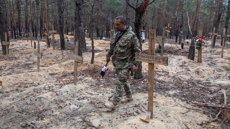 Ukrainian serviceman walks among graves of mostly unidentified civilians and Ukrainian soldiers at an improvised cemetery in the town of Izium