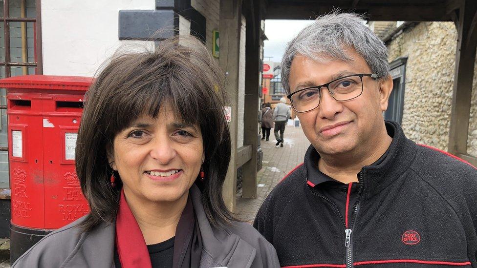 Rita and Ashwin Patel stand in their post office uniform in front of a red postbox